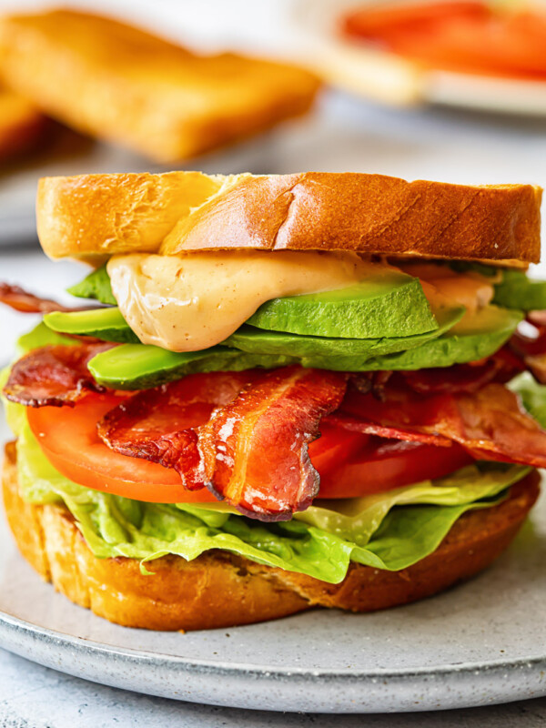 close up of BLT sandwich with avocado and sauce spilling over