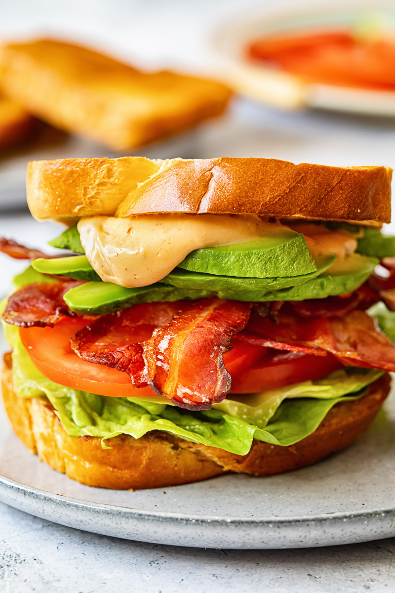 close up of BLT sandwich with avocado and sauce spilling over