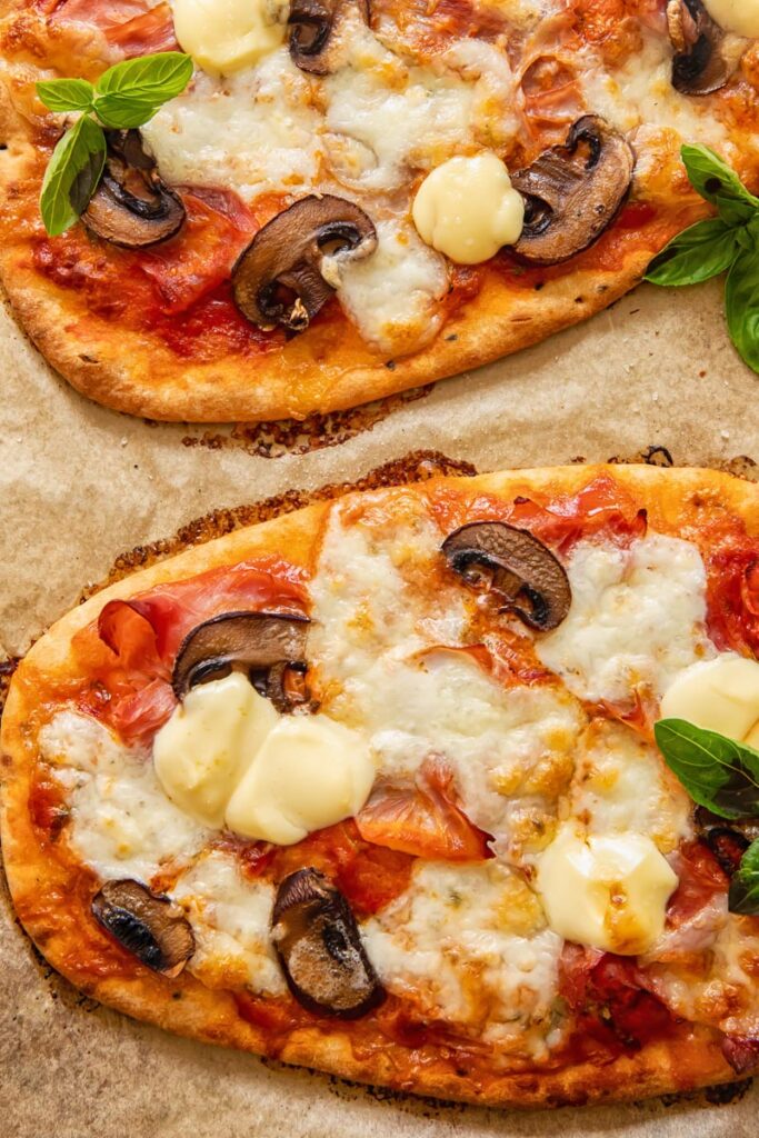 Naan pizza on baking sheet with mushrooms and cheese