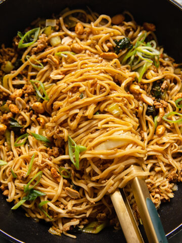 noodles in a black wok with tongs holding the noodles
