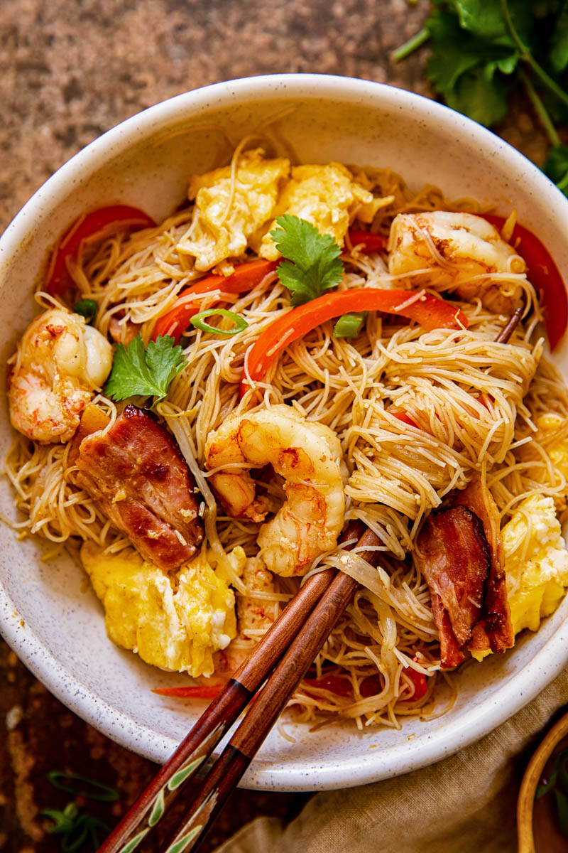 Stir fried rice noodles with prawns and red peppers in a bowl with chopsticks
