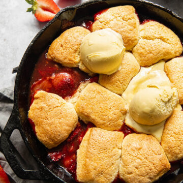 strawberry cobbler in a cast iron skillet, topped with ice cream