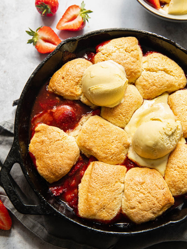 strawberry cobbler in a cast iron skillet, topped with ice cream