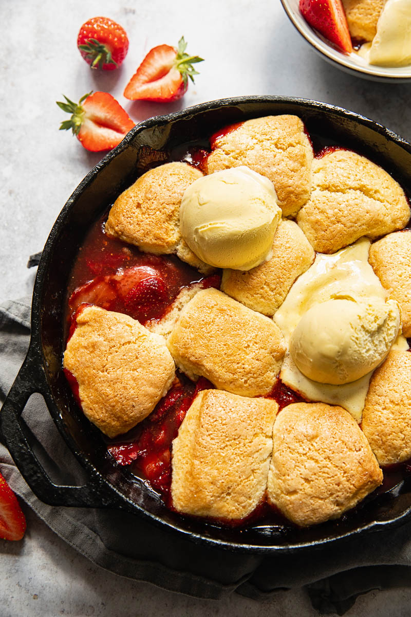strawberry cobbler in a cast iron skillet, topped with ice cream