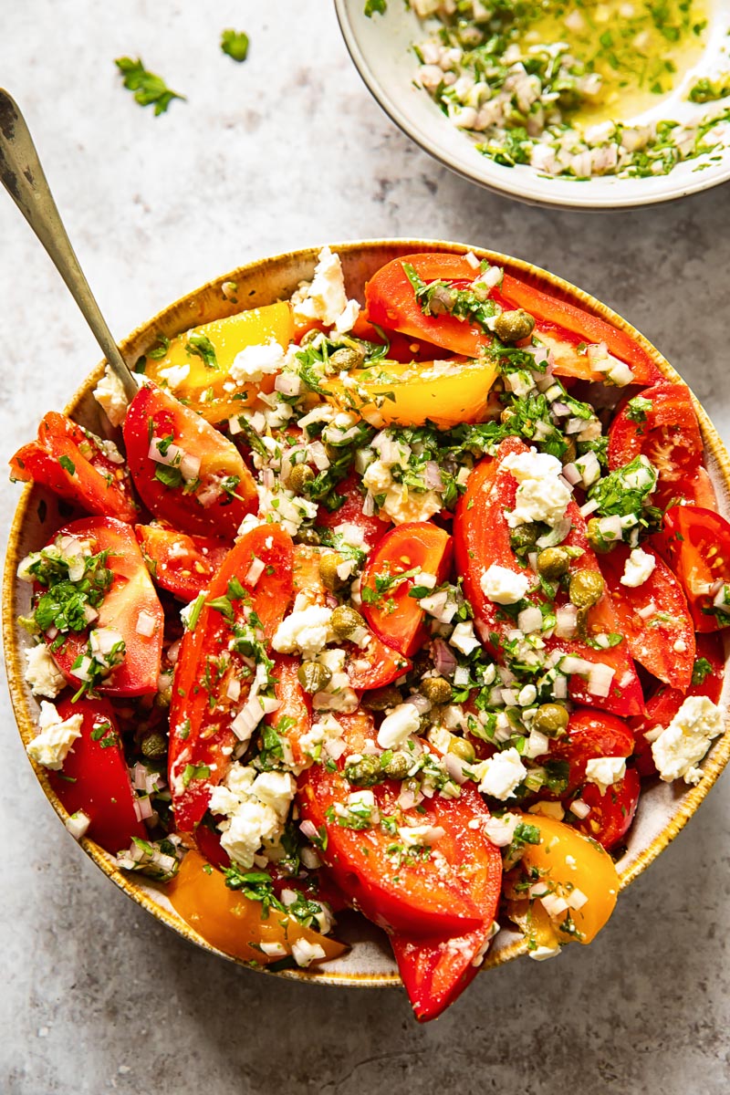 top down view of tomato salad in a bowl and herb vinaigrette in a smaller bowl