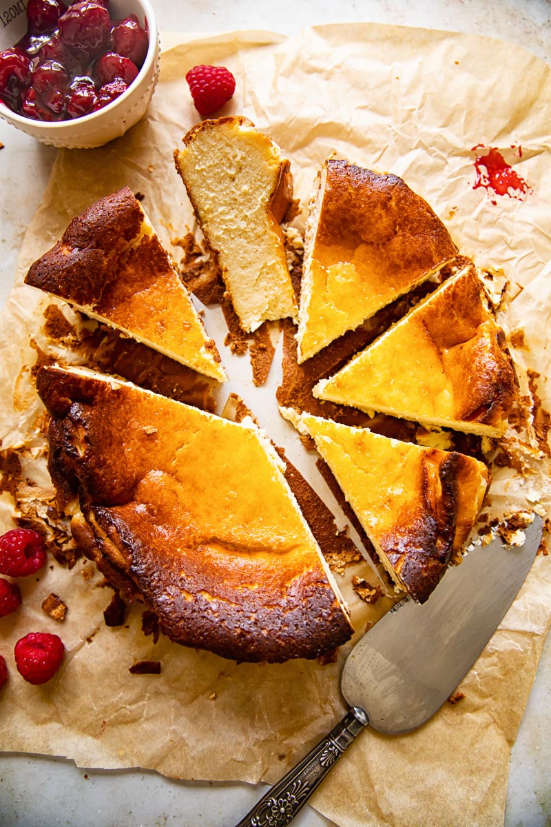 top down view of cheesecake cut into slices, a knife, raspberry compote