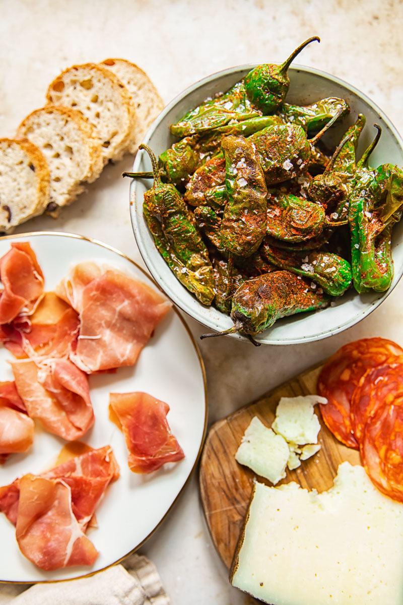 top down view of padron peppers, Serrano ham, chorizo and cheese on a board