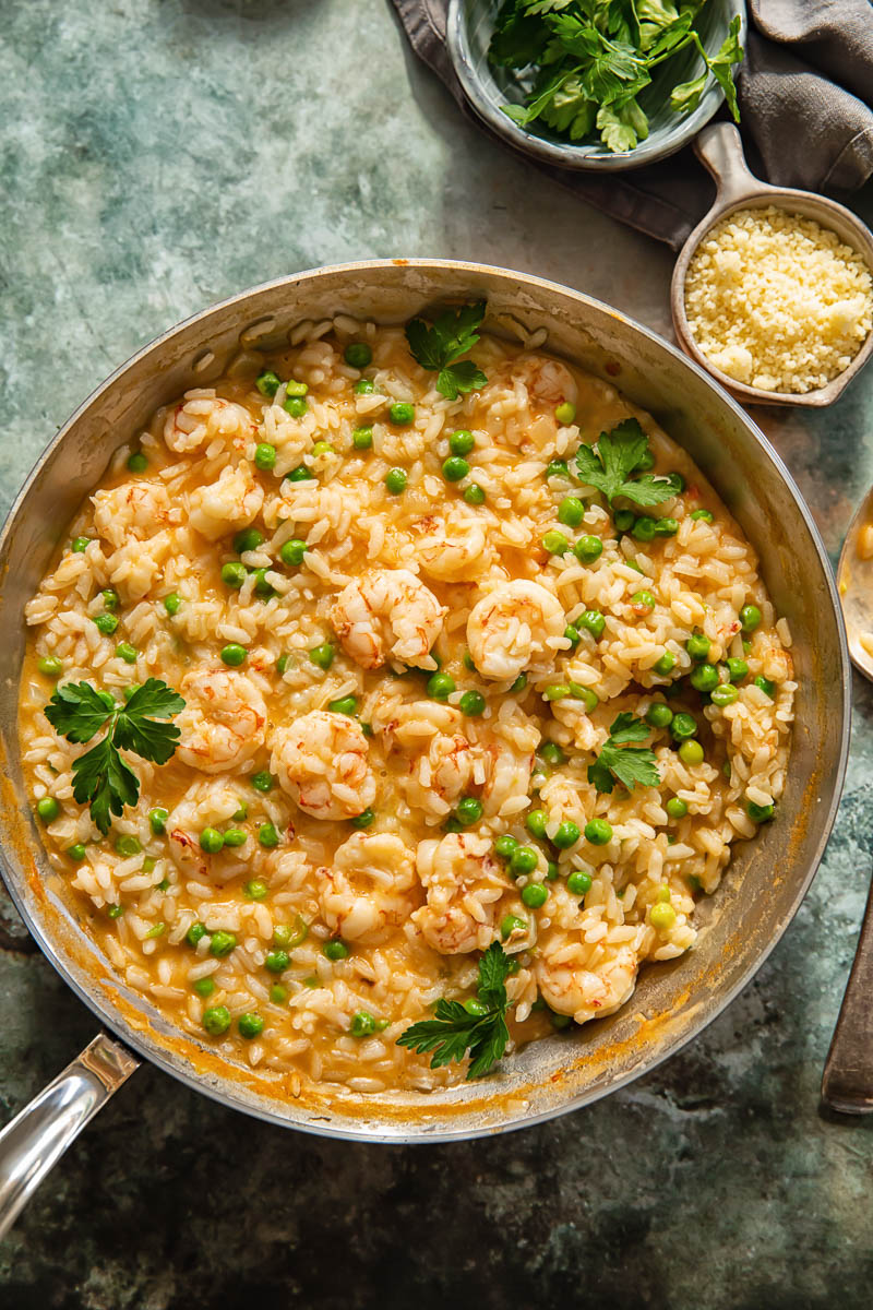 top down view of prawn risotto in a pan, two little bowls with Parmesan and parsley