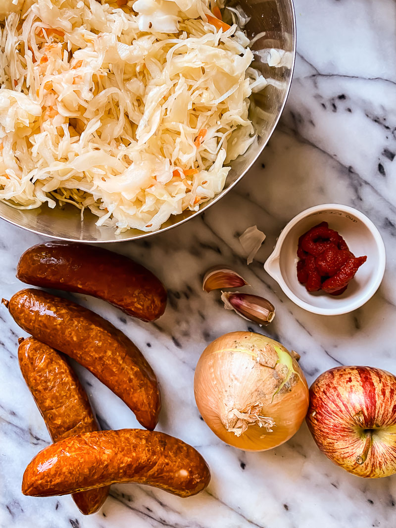 sauerkraut in a bow, kielbasa, an onion, an apple, tomato paste and garlic