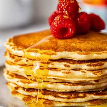 side view of a pancake stack topped with Maple syrup and raspberries