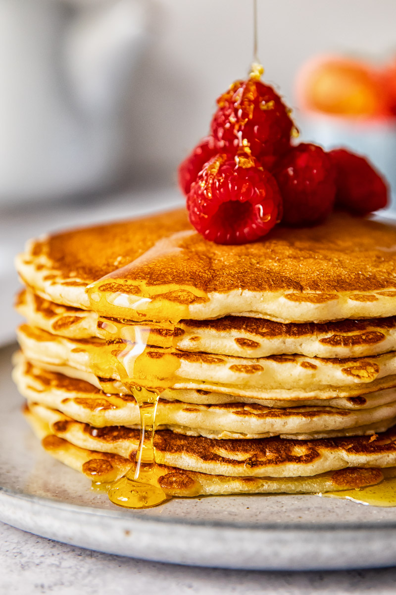 side view of a pancake stack topped with Maple syrup and raspberries