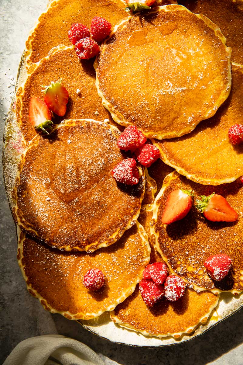 top down view of pancakes piled on a platter with berries scattered all over.