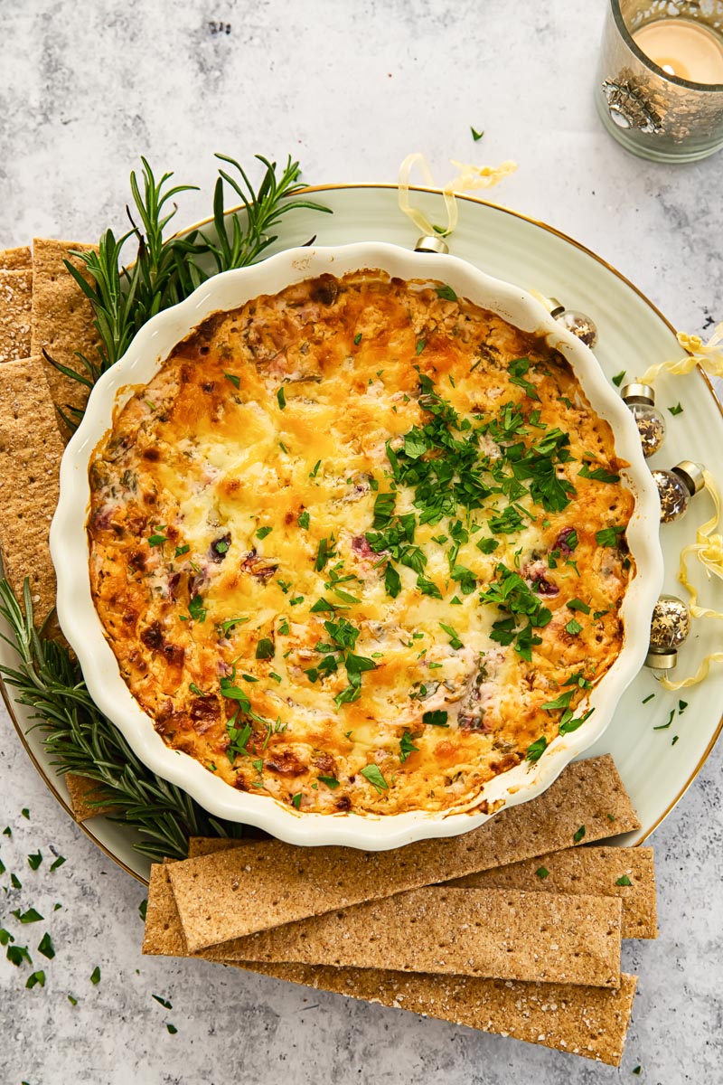 top down view of cheesy dip with chorizo and cranberries, cracker next to the dish