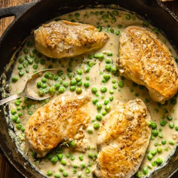 top down view of cast iron pan with chicken breasts and green peas in a creamy sauce