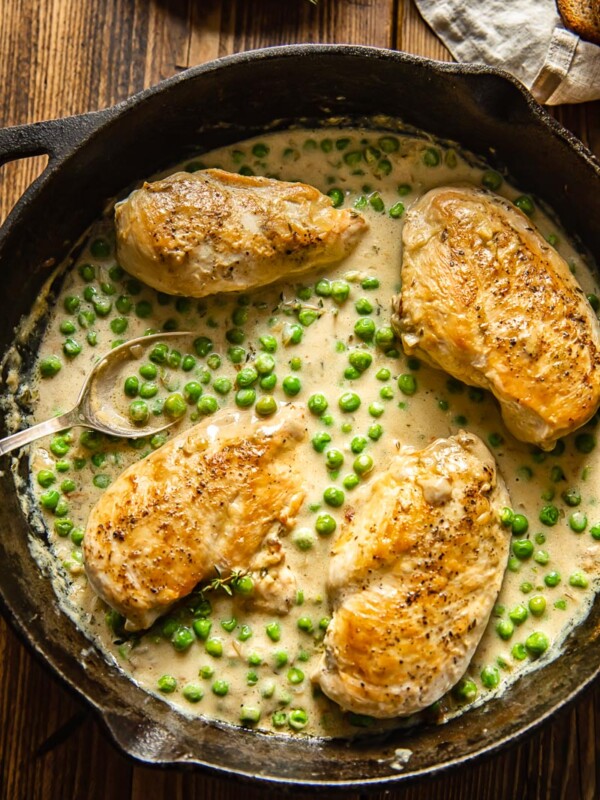 top down view of cast iron pan with chicken breasts and green peas in a creamy sauce