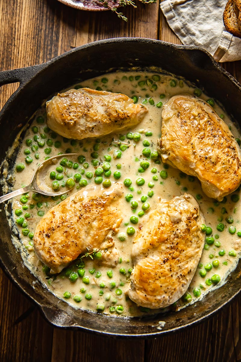 top down view of cast iron pan with chicken breasts and green peas in a creamy sauce