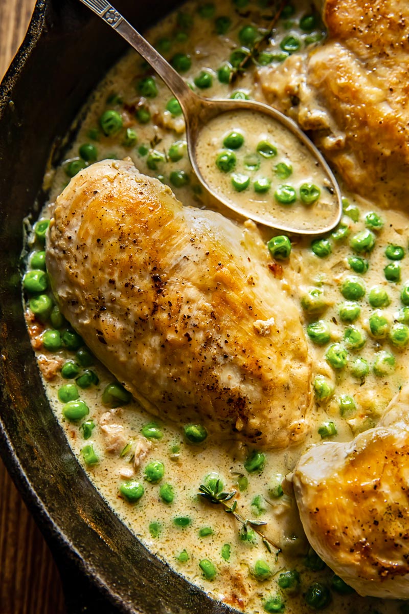 close up of chicken breast in a creamy sauce with green peas
