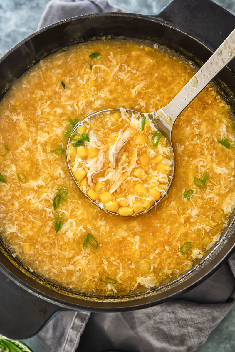 egg drop soup with chicken in a soup pot with a ladle in it.