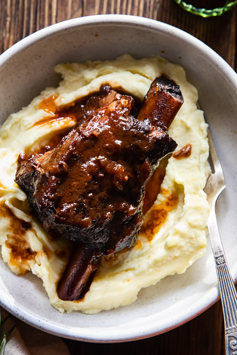 beef short rib in red wine sauce on top of mashed potatoes in a bowl