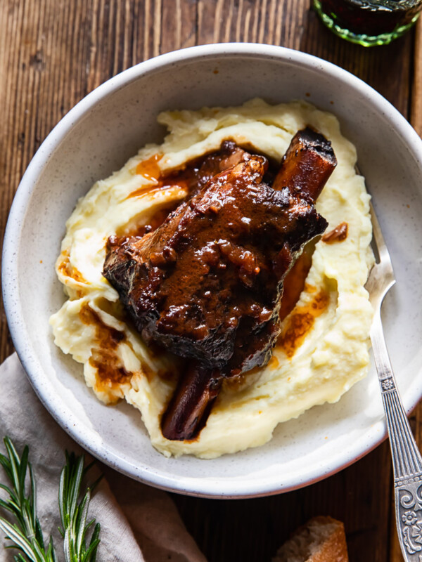 top down view of a braised short rib on top of mashed potatoes in a bowl, a glass of wine next to it
