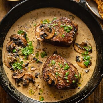 top down view of 2 filet mignon steaks in a mushroom sauce in a cast iron pan