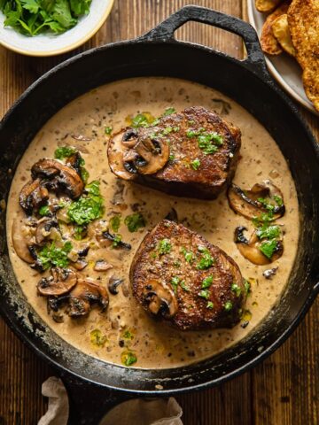 top down view of 2 filet mignon steaks in a mushroom sauce in a cast iron pan