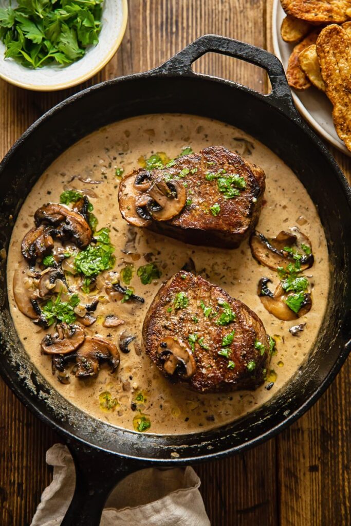 top down view of 2 filet mignon steaks in a mushroom sauce in a cast iron pan