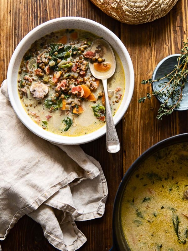 a soup pot, a soup bowl with a napkin next to it, fresh thyme and a loaf of bread on a table