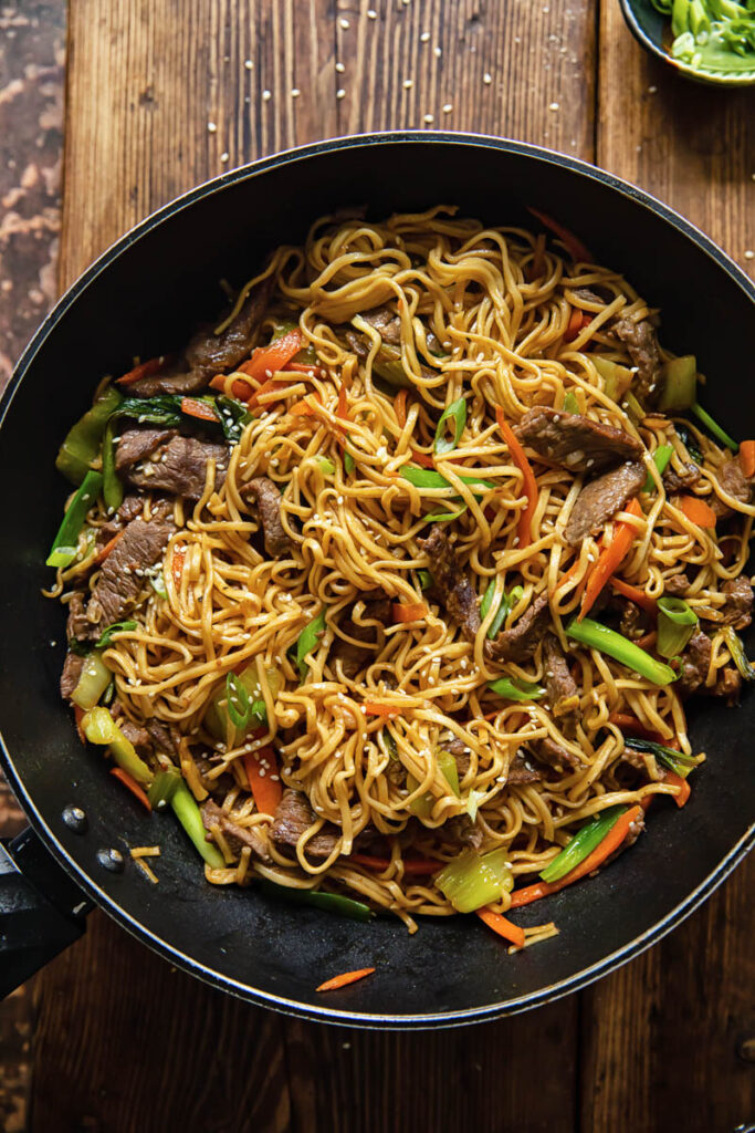 top down view of Asian noodles dish with beef and vegetables in a wok