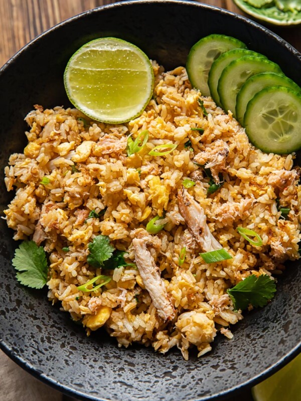 crab fried rice with sliced cucumbers and a lime wedge in a dark bowl