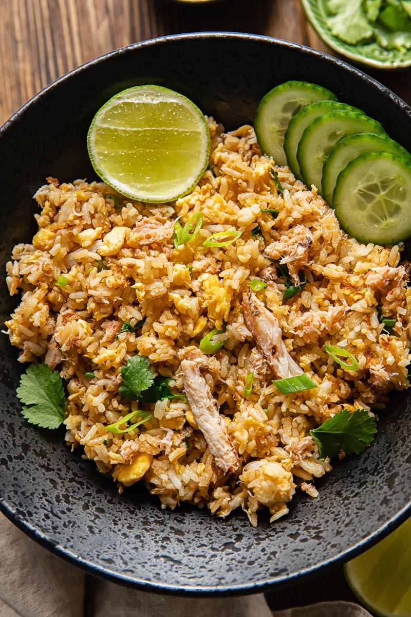 crab fried rice with sliced cucumbers and a lime wedge in a dark bowl