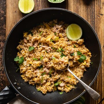 top down view of fried rice in a wok, a green bowl with greens and a green bowl with sliced red chilli next to the wok