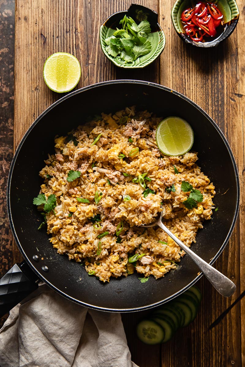 top down view of fried rice in a wok, a green bowl with greens and a green bowl with sliced red chilli next to the wok