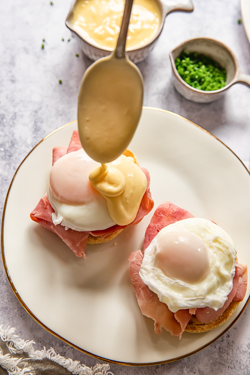 hollandaise sauce being dolloped on a poached egg
