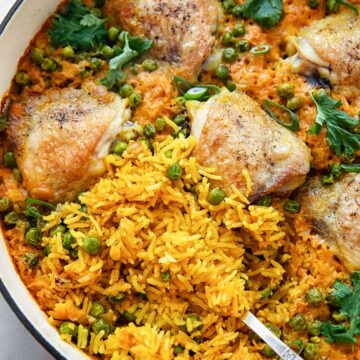 top down view of chicken thigh and yellow turmeric rice casserole with green peas