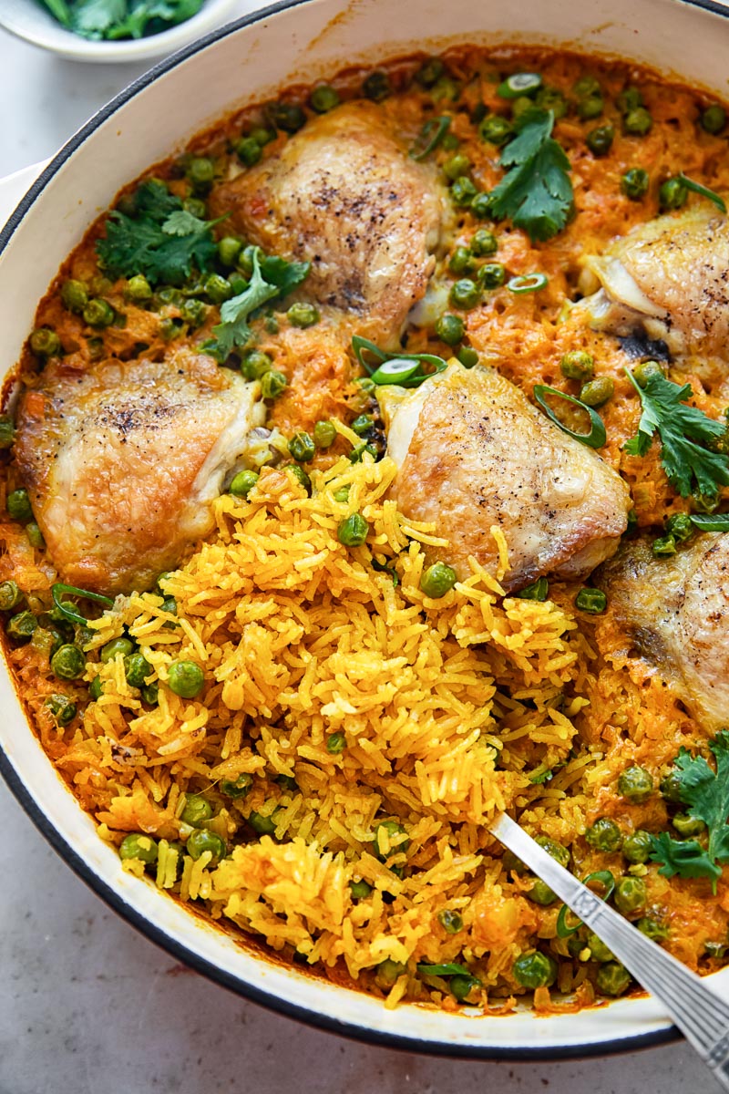 top down view of chicken thigh and yellow turmeric rice casserole with green peas