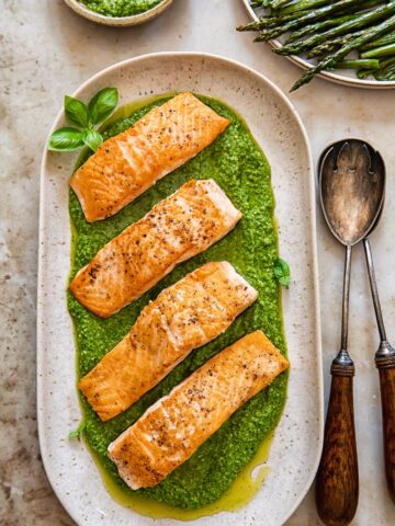 top down view of salmon fillets on top of pesto on a beige platter