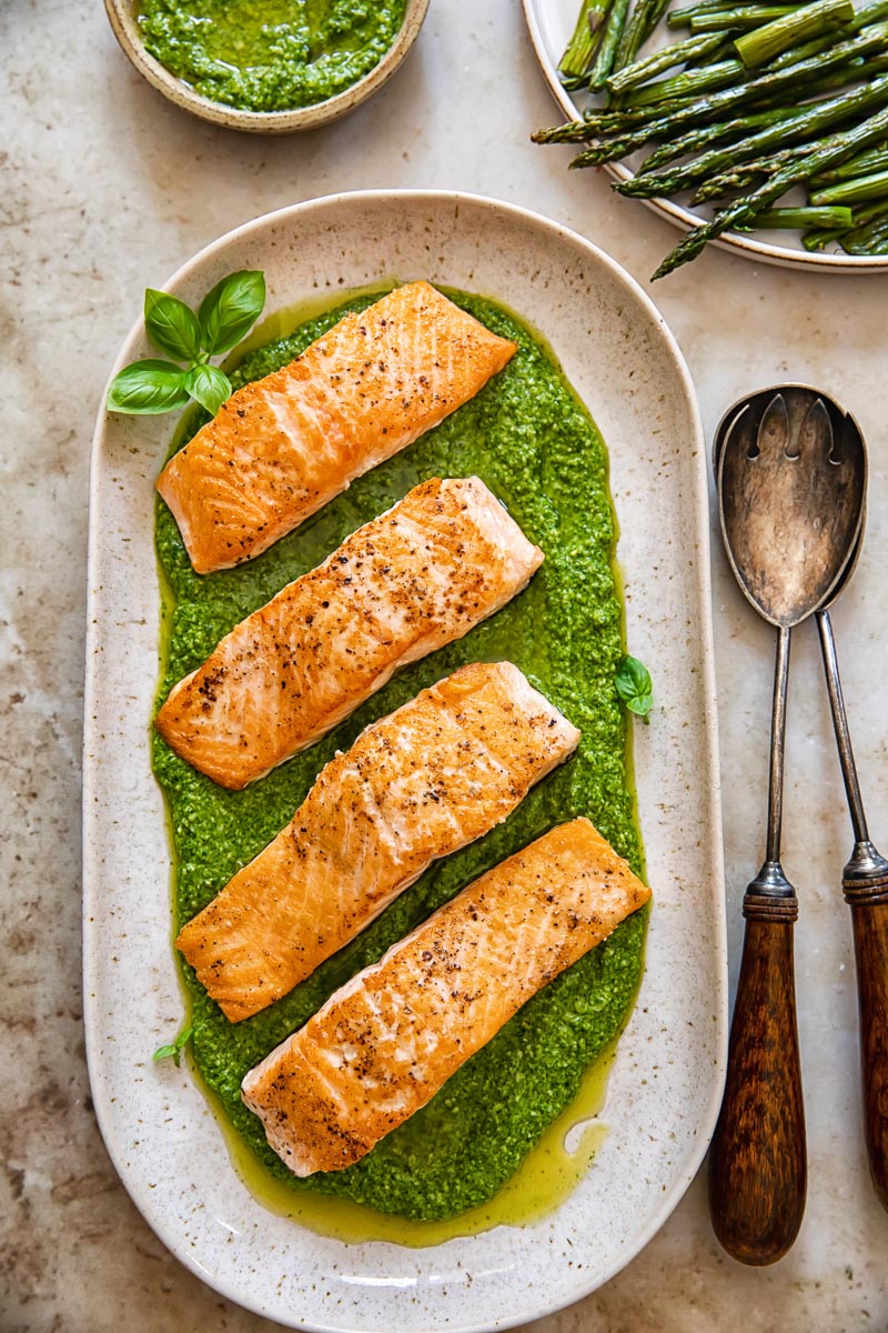 top down view of salmon fillets on top of pesto on a beige platter