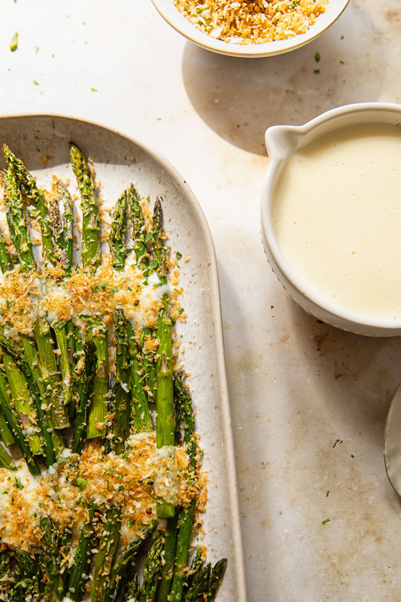 asparagus with breadcrumbs on a platter and cheese sauce in a bowl
