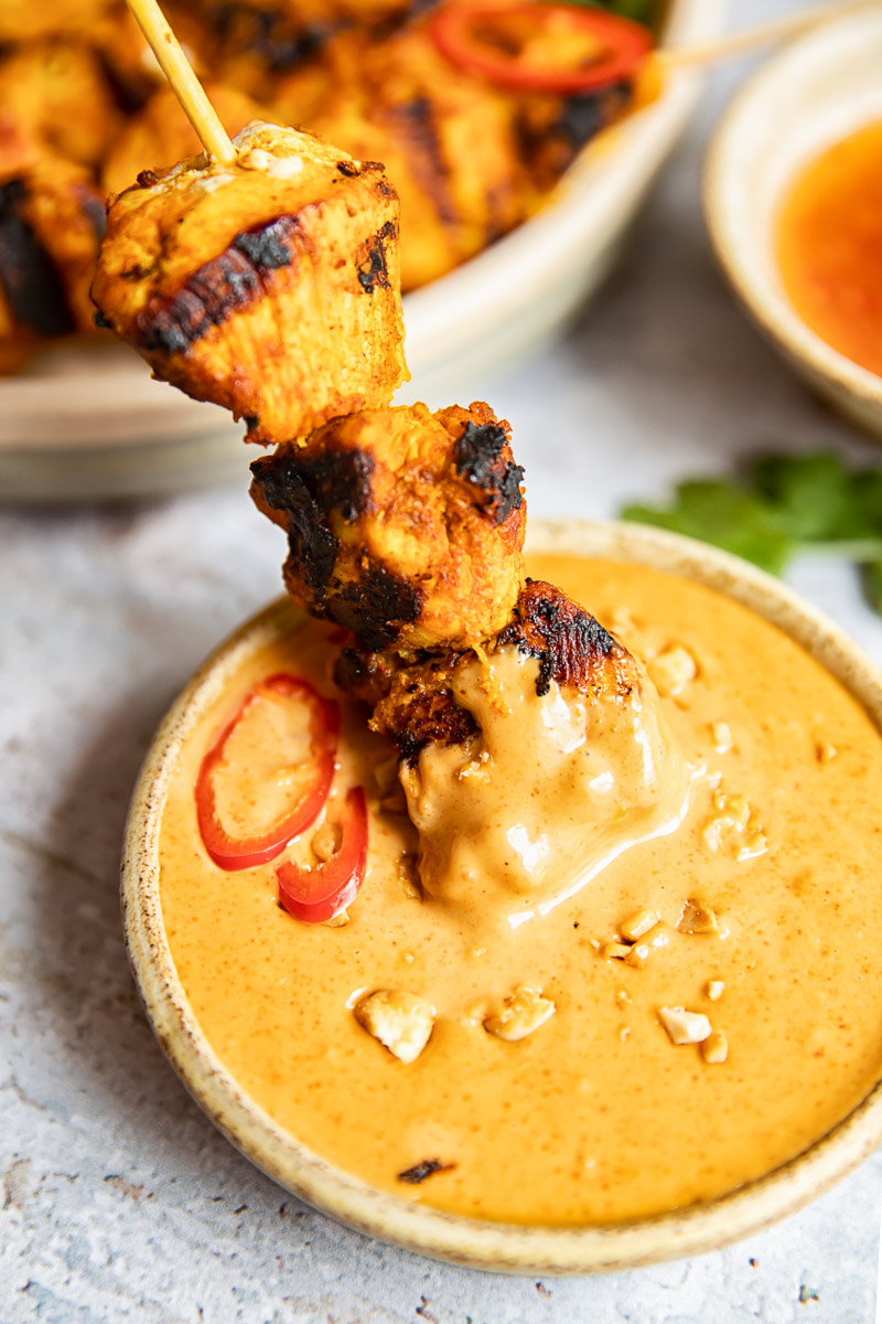 chicken skewer being dipped in peanut sauce