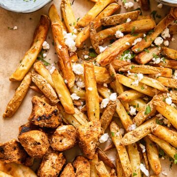 top down view of fries topped with feta, grilled chicken bites, pita and yogourt dip