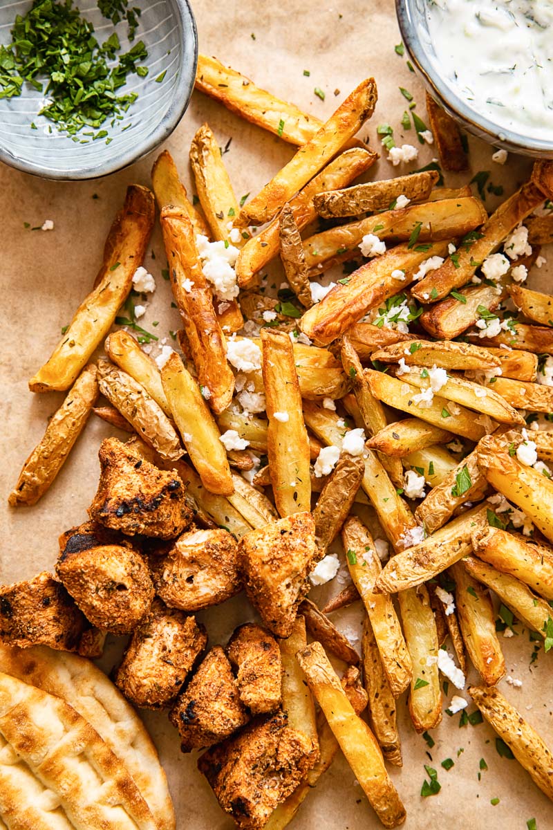 top down view of fries topped with feta, grilled chicken bites, pita and yogourt dip