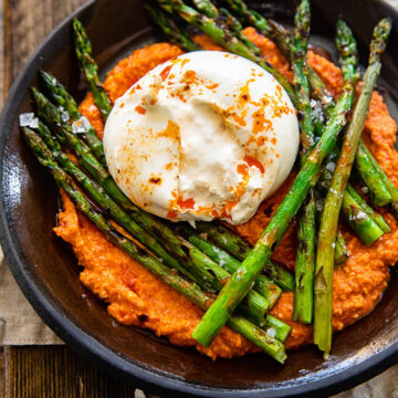 top down view of grilled asparagus on top with romesco sauce and burrata cheese on a brown plate