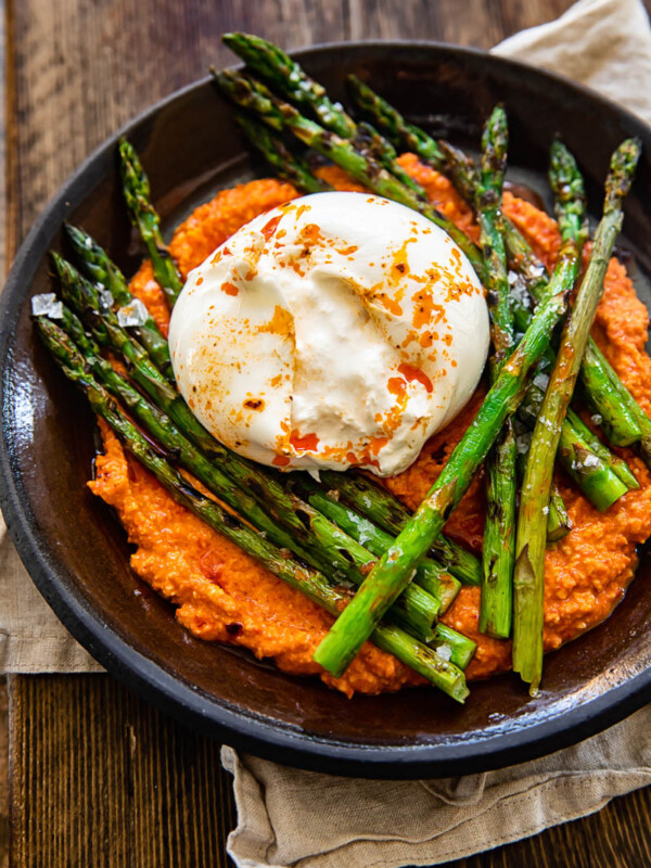 top down view of grilled asparagus on top with romesco sauce and burrata cheese on a brown plate