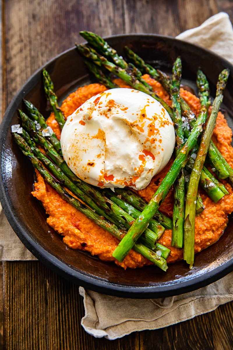 top down view of grilled asparagus on top with romesco sauce and burrata cheese on a brown plate