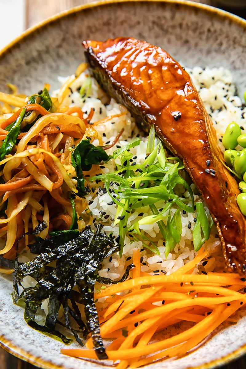 close up of rice bowl topped with salmon, stir fried vegetables and other toppings