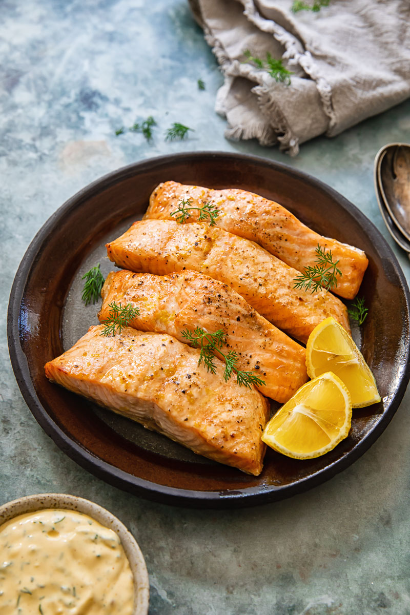 top down view of salmon on a plate, lemon dill sauce and a napkin