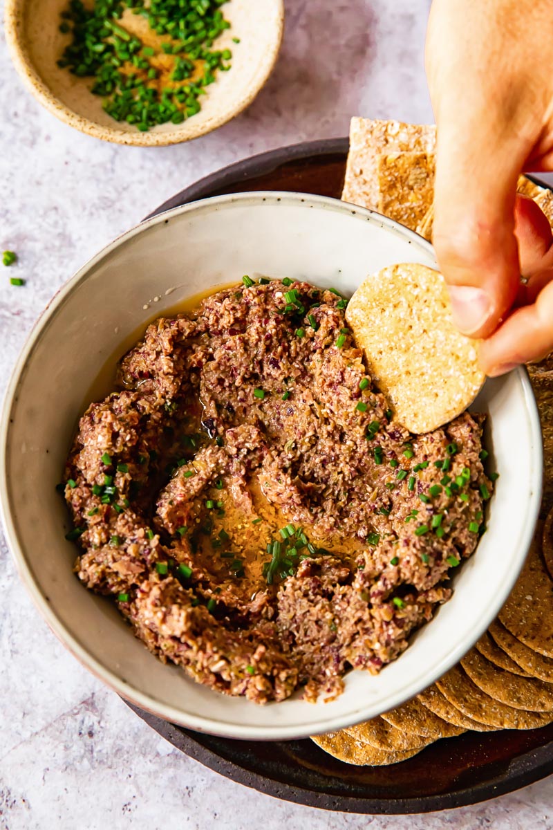 a cracker being dipped into tapenade