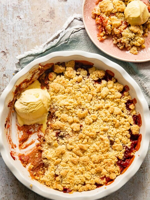 top down view of rhubarb crumble with vanilla ice cream in a pan and on a pink plate
