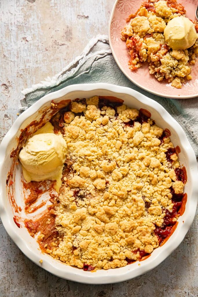 top down view of rhubarb crumble with vanilla ice cream in a pan and on a pink plate